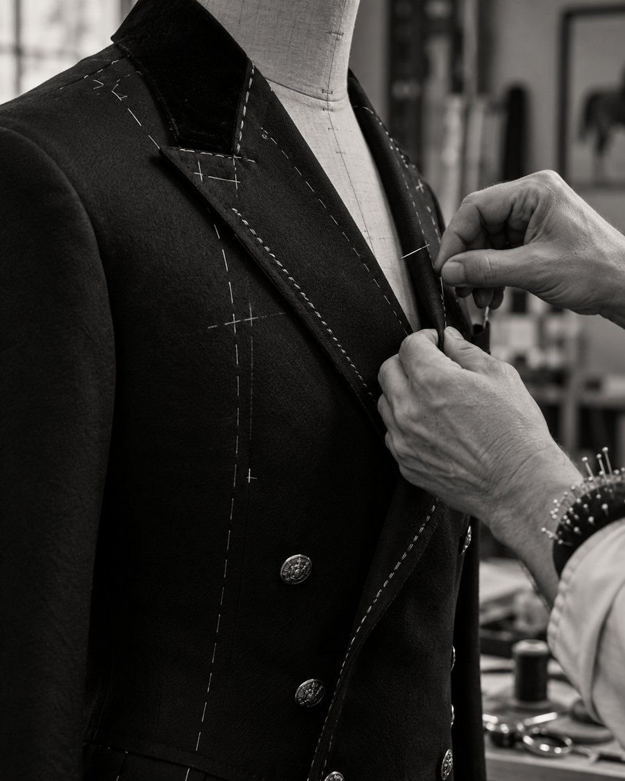 Tailor's hands pinning a bespoke coat lapel on a mannequin, basting stitches and chalk marks visible